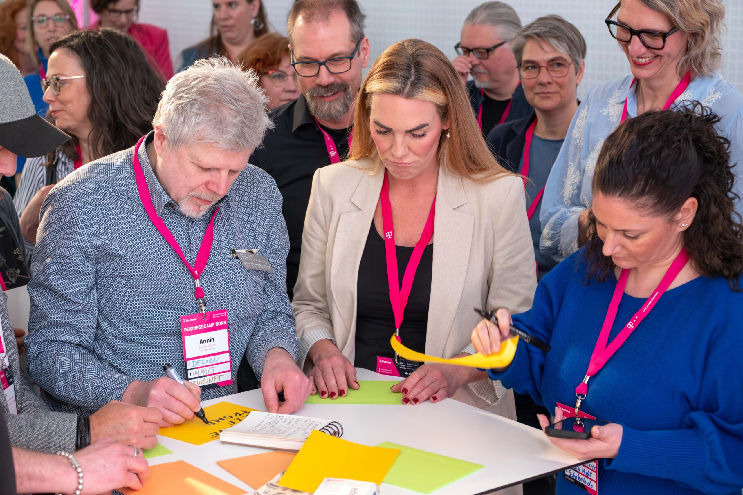 Eine bunte Gruppe von Menschen, die gemeinsam an einem Tisch stehen, umgeben von bunten Post-its, auf die Sessiontitel geschrieben werden.